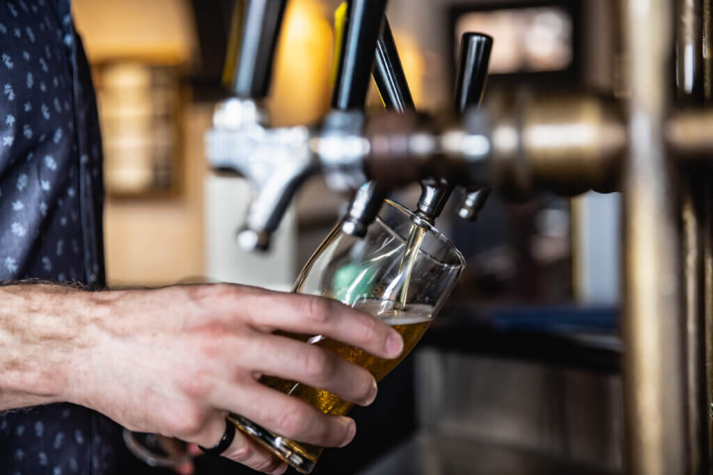 Close-up of bartender tilting a glass while pouring golden beer from a tap system.