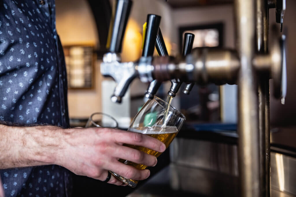 Bartender holding a tilted glass under a beer tap, pouring a fresh draught with precision.