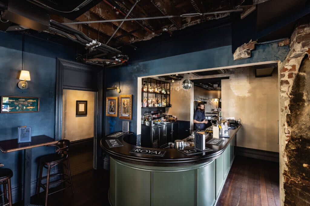Small boutique bar with curved counter, intimate seating and bartender serving drinks at The Royal.