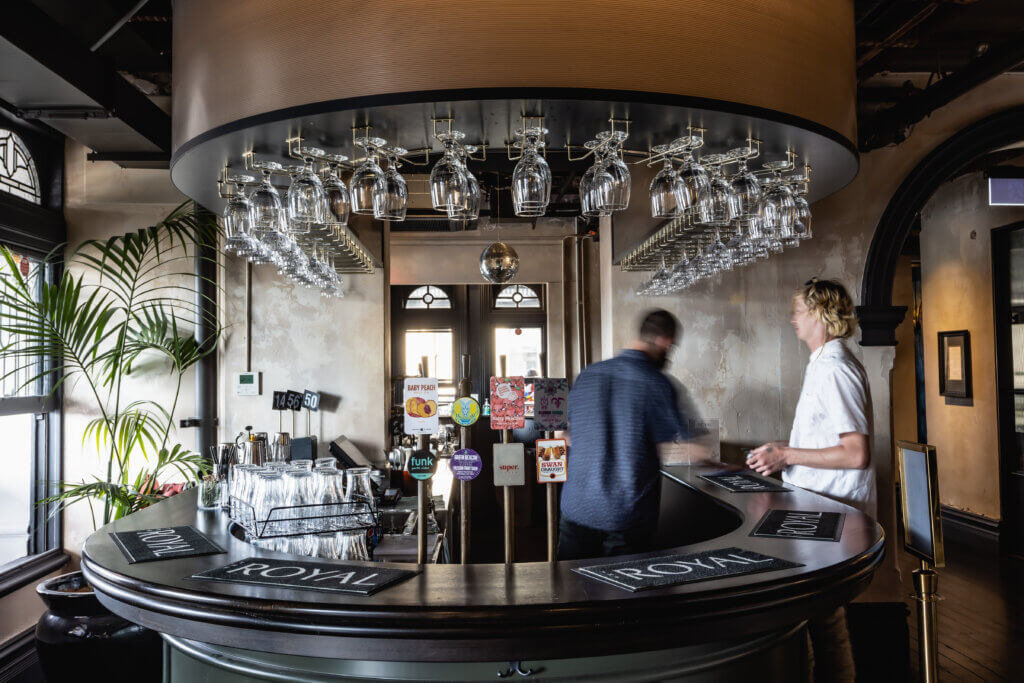 Close-up of curved bar with hanging glassware and tap handles featuring local craft beers, served by a bartender.