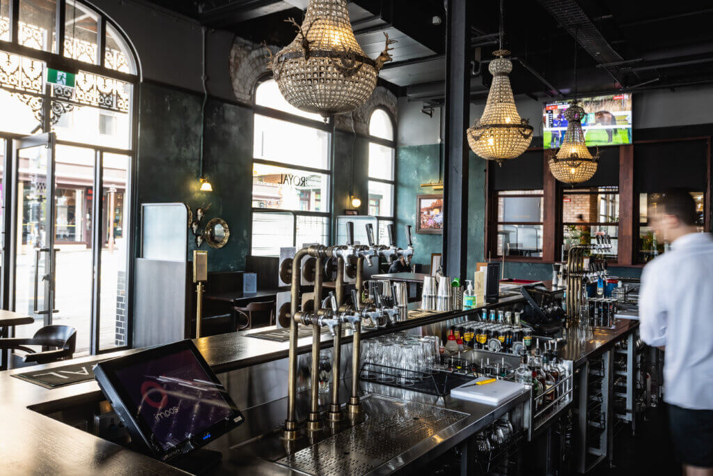 Modern bar interior with stainless steel beer taps, glassware and chandeliers, featuring professional beverage fitout.