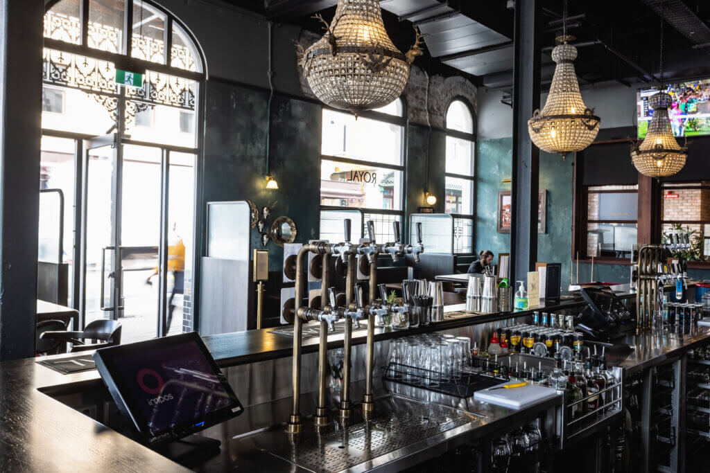 Modern bar interior with stainless steel beer taps, glassware and chandeliers, featuring professional beverage fitout.