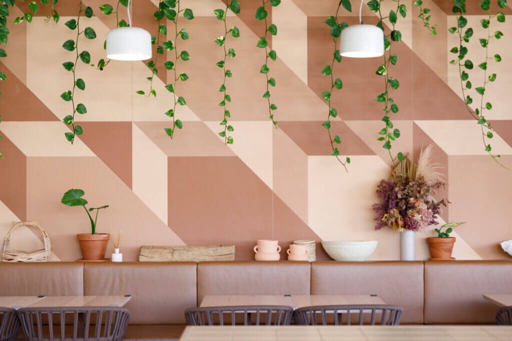 Modern café interior with geometric pink wall, hanging greenery and minimalist décor on a tan leather bench seat.
