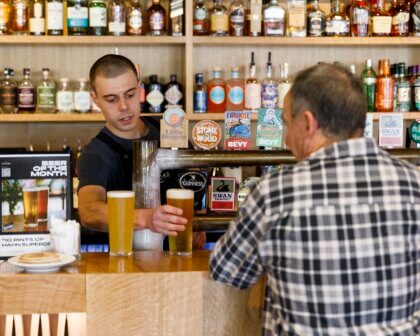 Bartender serving pints of beer to customer at The Elford bar, with spirits displayed on shelves behind.