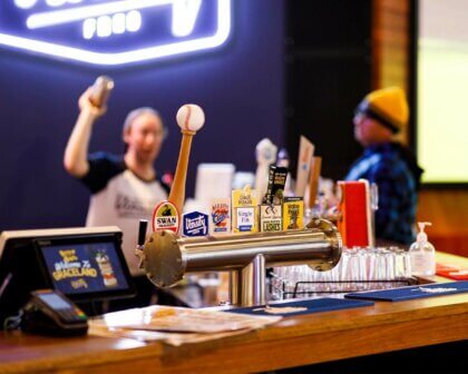 Bar counter with branded beer taps at Varsity venue, bartender celebrating in the background.