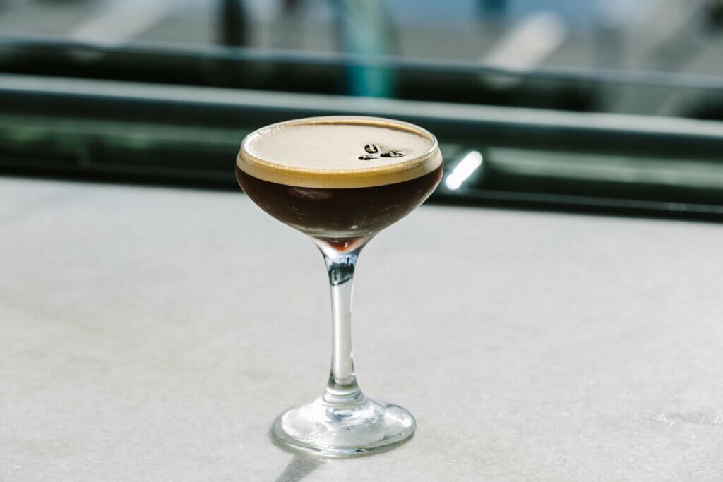 Espresso martini cocktail in a coupe glass with coffee bean garnish on marble surface.