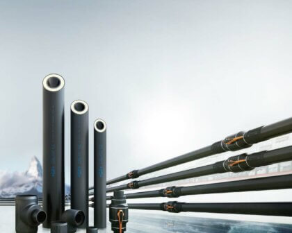 Industrial insulated pipes and fittings displayed on icy surface with mountain backdrop.