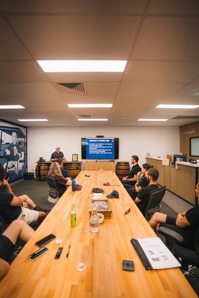 Team training session at Barons with older man presenting chemical handling guidelines on screen.