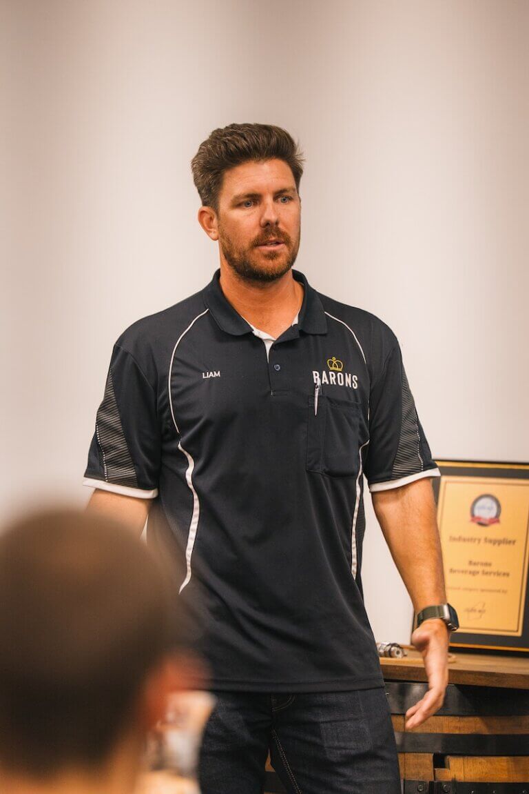 Man in Barons polo shirt presenting during a workplace training session, with industry award in background.
